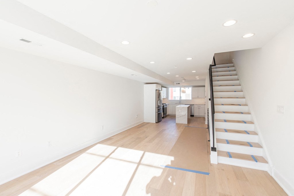 a living room with a staircase and white walls and wood floors