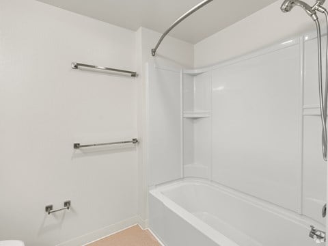 A white bathroom with a tub, towel rack, and shower head.