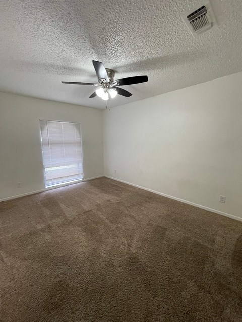 an empty living room with a ceiling fan and a window