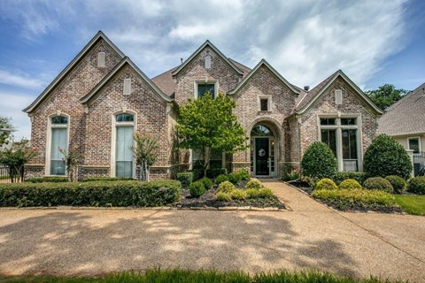 the front of a brick house with a driveway and trees