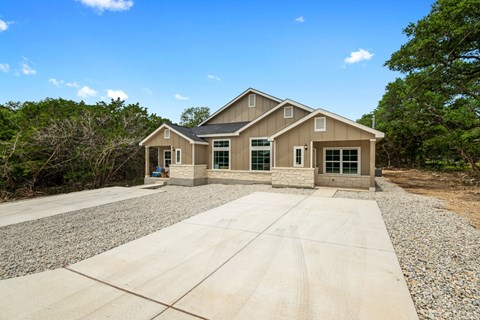 a home with a concrete driveway and a house in the woods