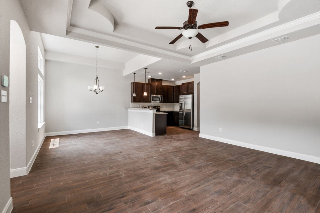 an empty living room with a ceiling fan and a kitchen