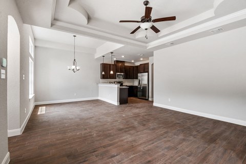 an empty living room with a ceiling fan and a kitchen