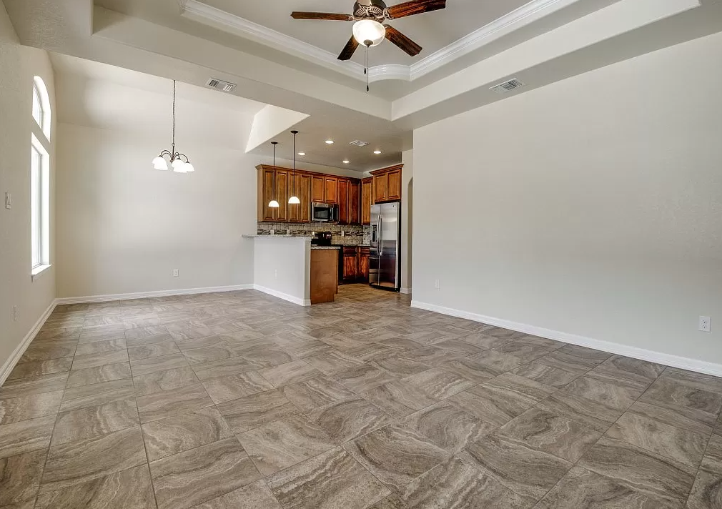 an empty living room with a kitchen and a ceiling fan
