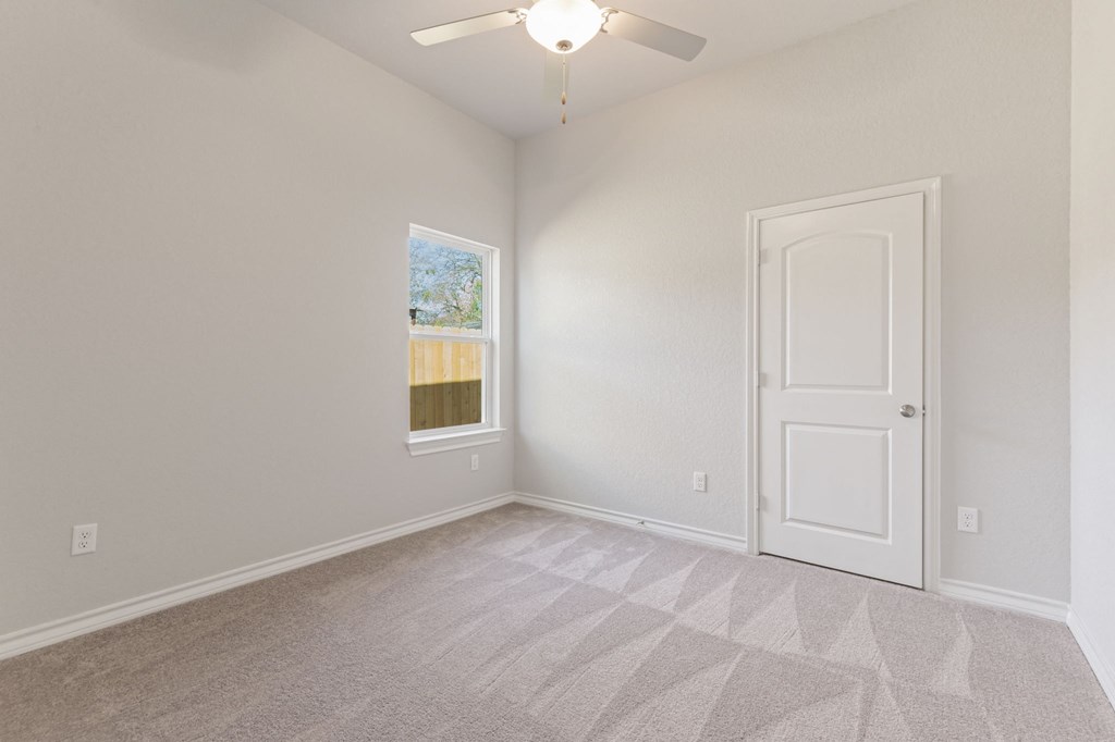 an empty bedroom with a white door and a ceiling fan