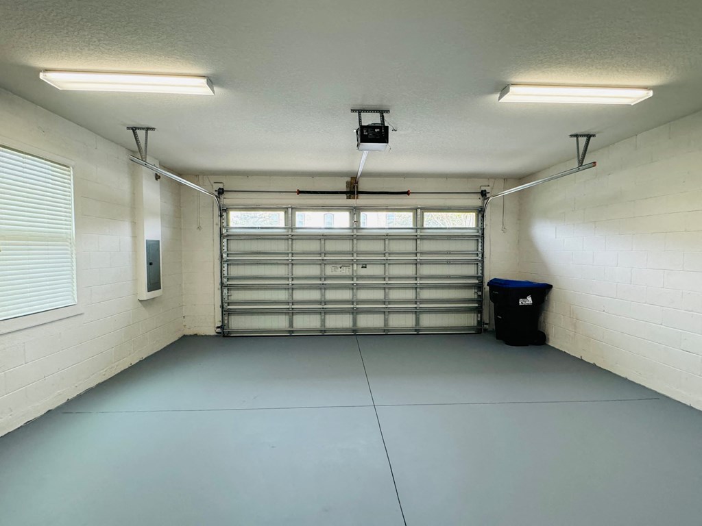 a large white room with a garage door and a trash can