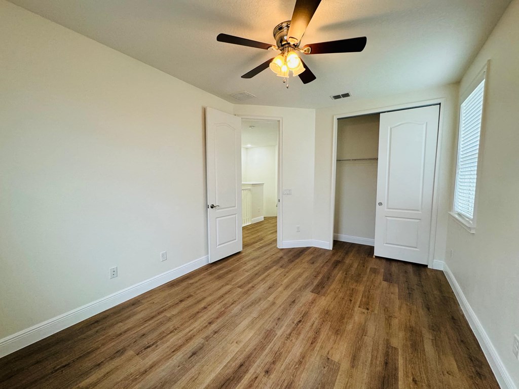 an empty living room with a ceiling fan and a closet