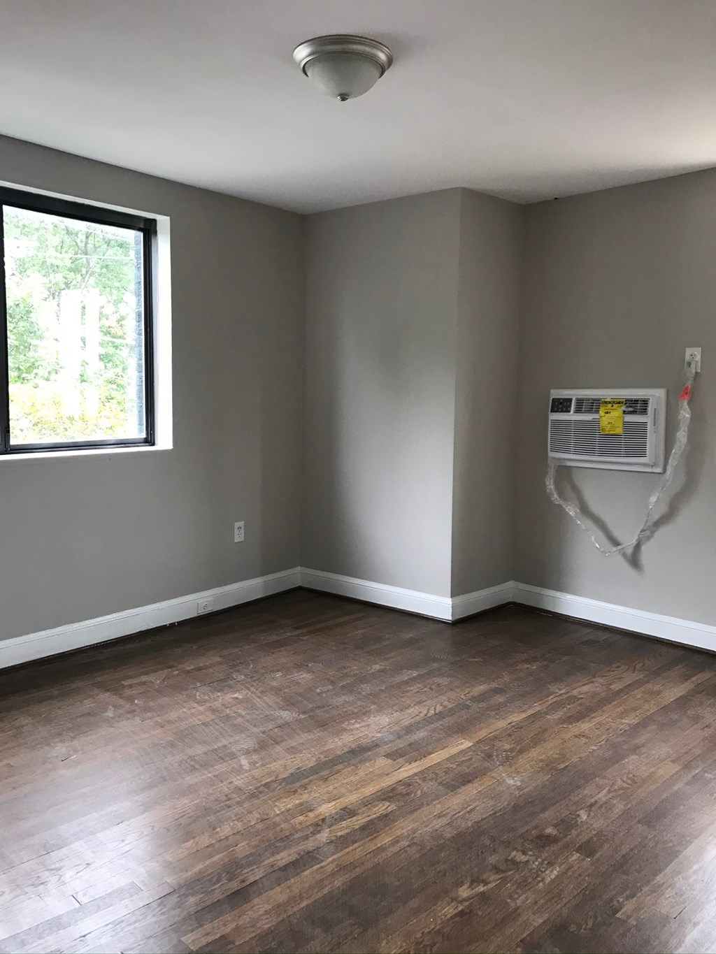 an empty room with gray walls and a window and wooden floors
