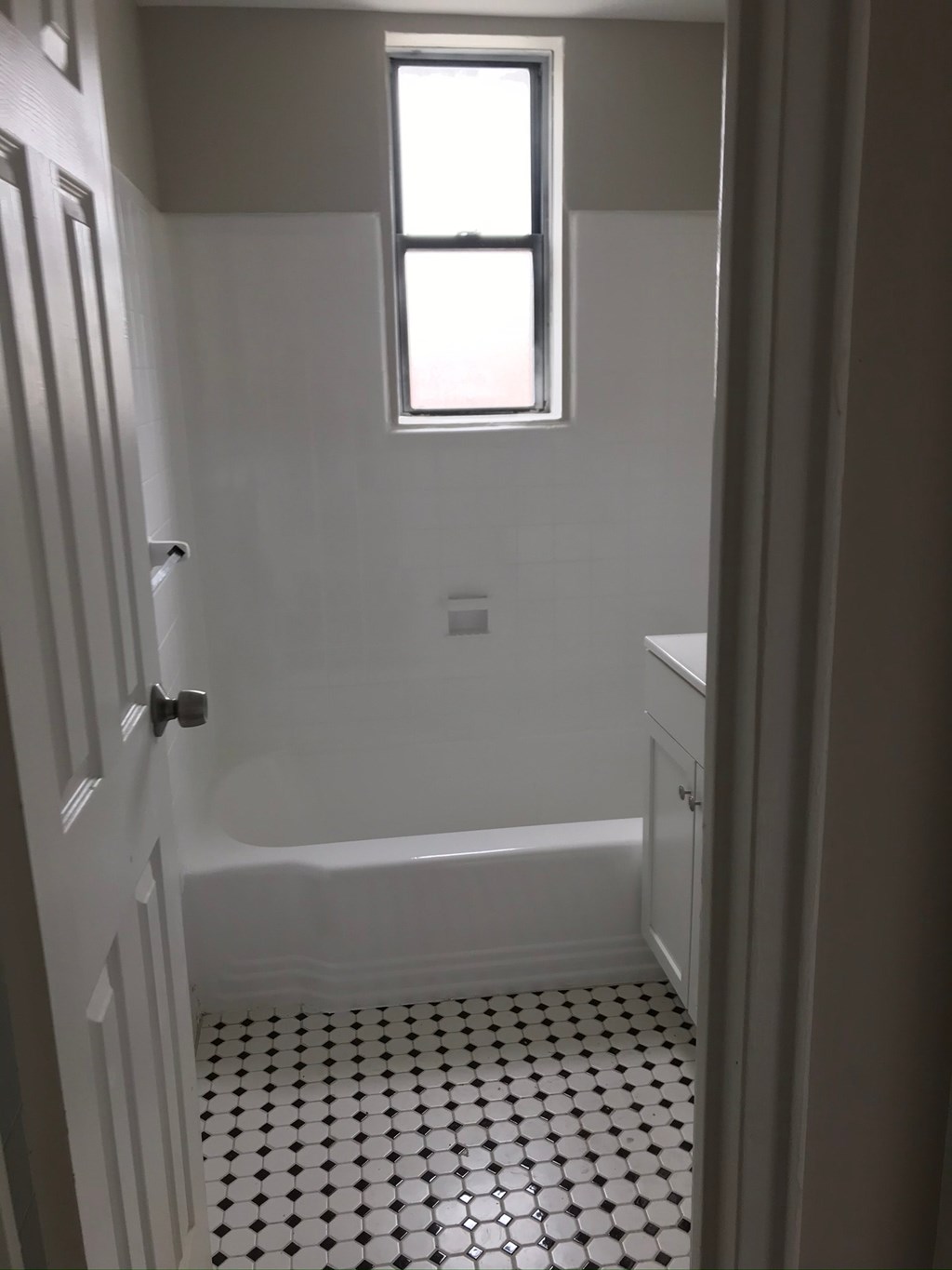 a white bathroom with a window and a white and black tiled floor