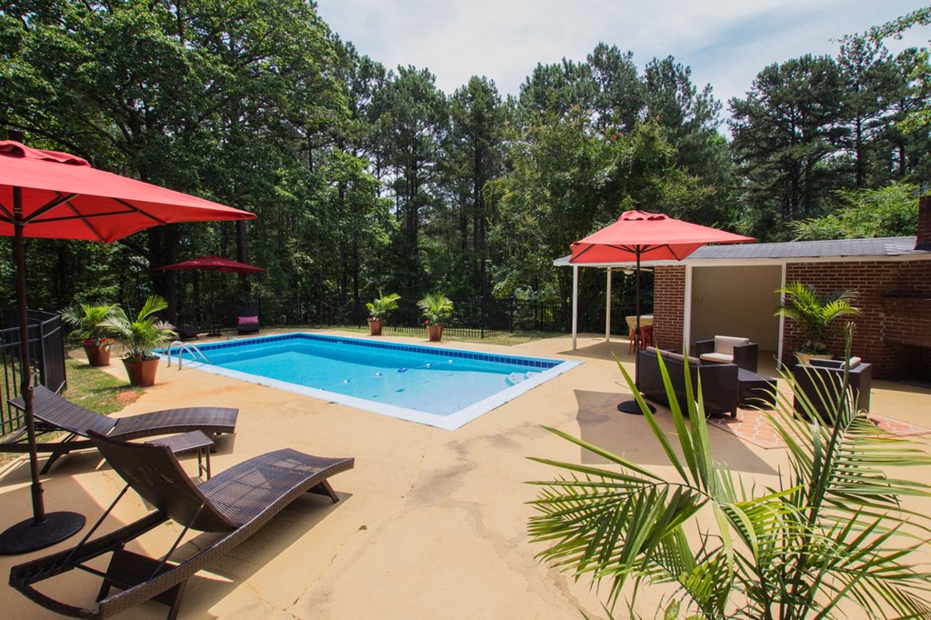 a swimming pool in a backyard with chairs and umbrellas