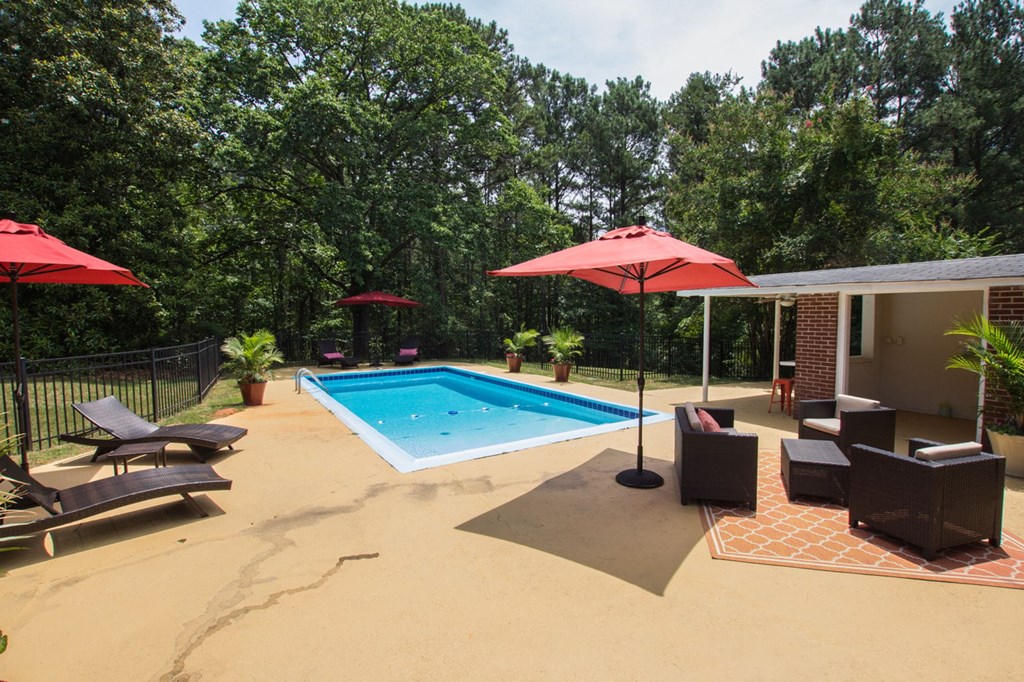 a pool in the backyard of a house with chairs and umbrellas