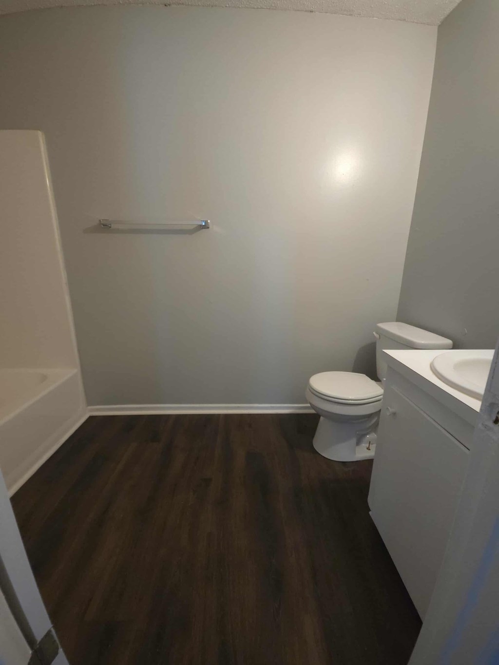 A white toilet sits in a bathroom with wood flooring.