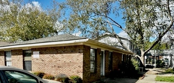 A small brick house with a porch and a car parked in front.
