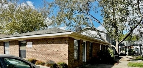 A small brick house with a porch and a car parked in front.