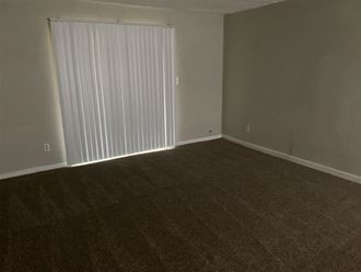 an empty living room with a large window with blinds