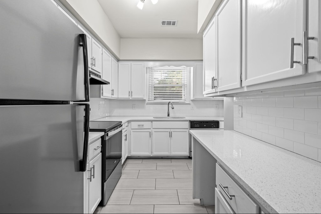 A black and white photo of a kitchen with white cabinets and a black fridge.