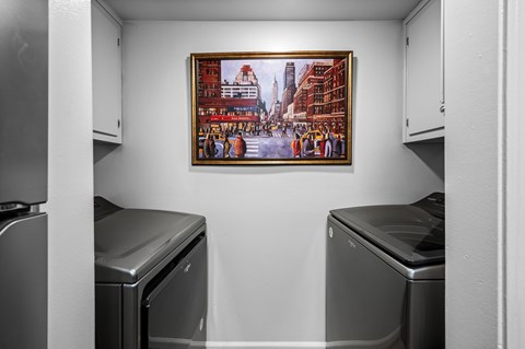 A framed picture of a cityscape hangs on a wall above two dishwashers in a kitchen.