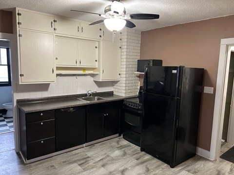 a kitchen with black appliances and white cabinets and a ceiling fan