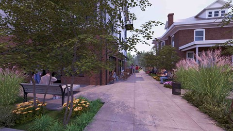 A street with people sitting on benches and houses on the side.