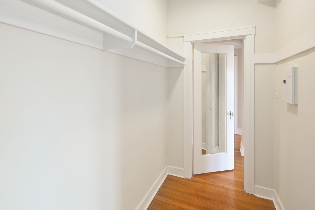 a hallway with white walls and a wood floor and a door to a closet