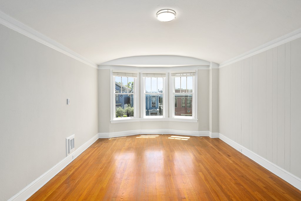 an empty living room with a wood floor and three windows