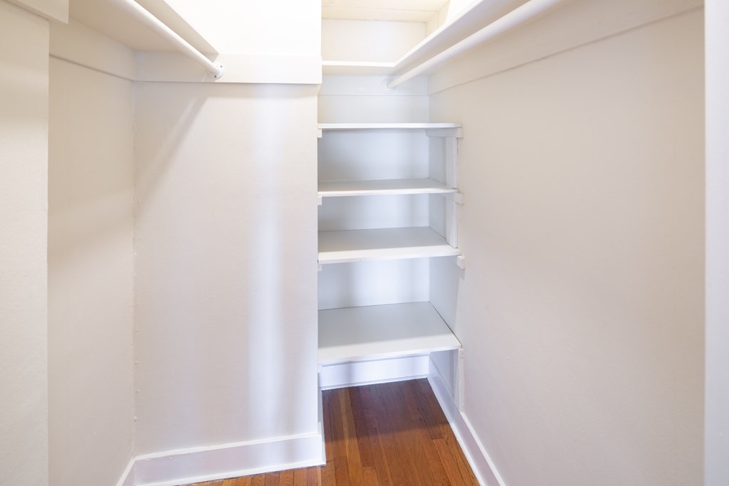 a walk in closet with white walls and shelves and a wood floor