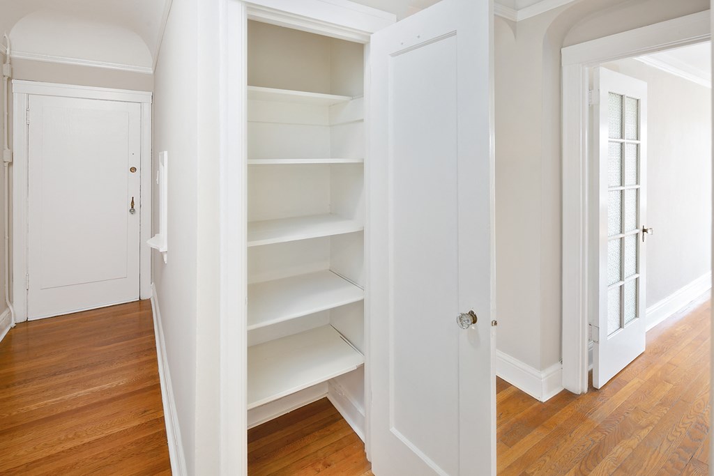 a closet with white shelves and a door and a wood floor