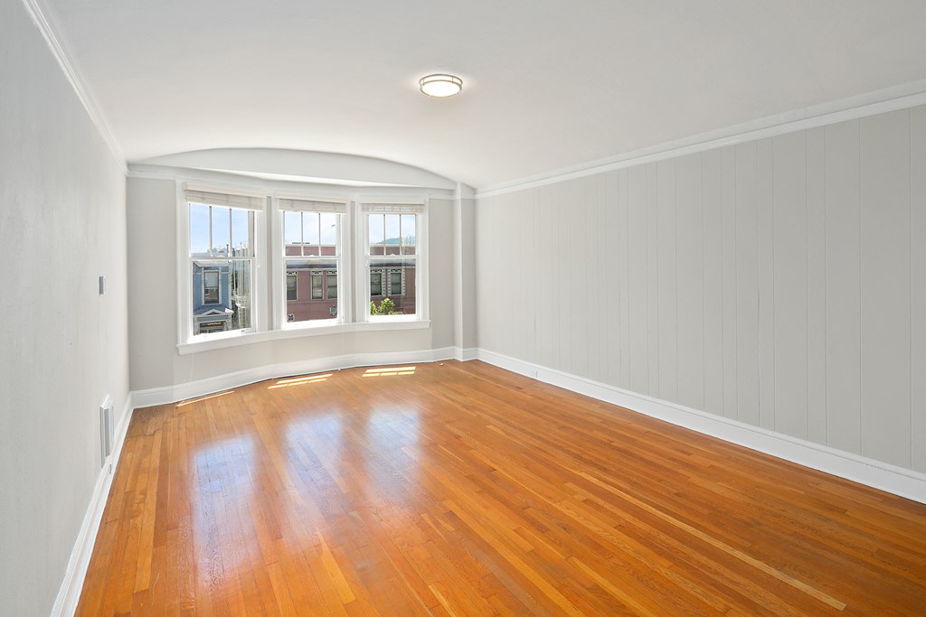 an empty living room with wood floors and a bay window