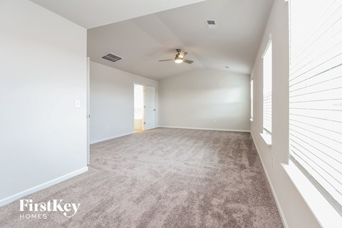 a spacious living room with white walls and carpet and a ceiling fan
