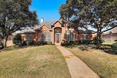 the front of a brick house with trees and a sidewalk