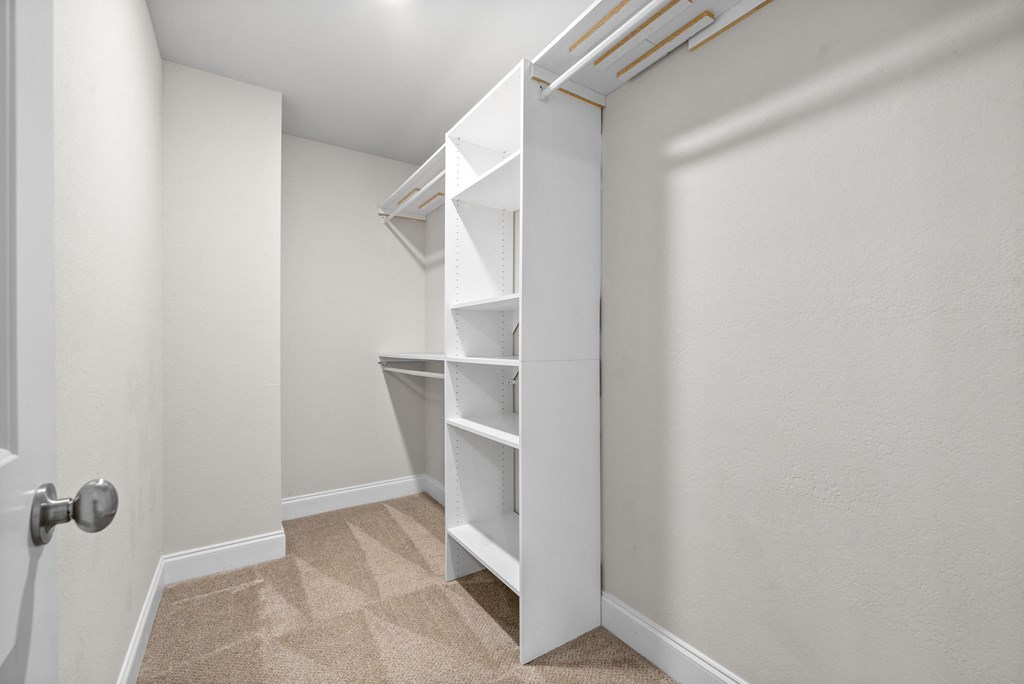a walk in closet with white shelves and a closet door