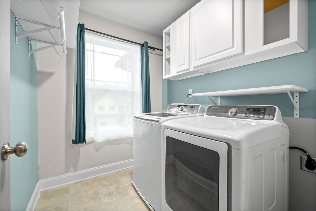 a washer and dryer in a laundry room with a window and white cabinets