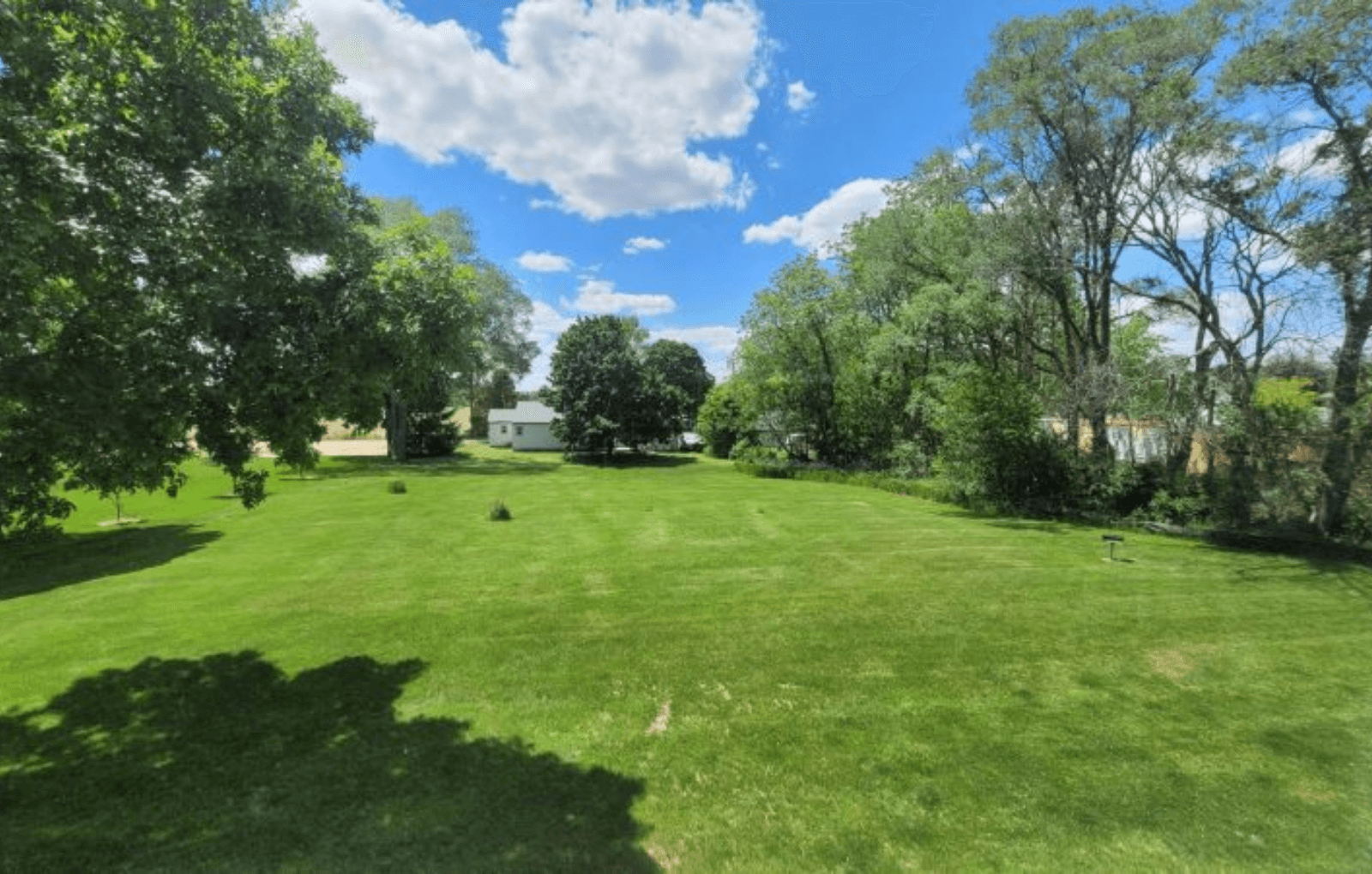 a large grass field with trees and a house in the background