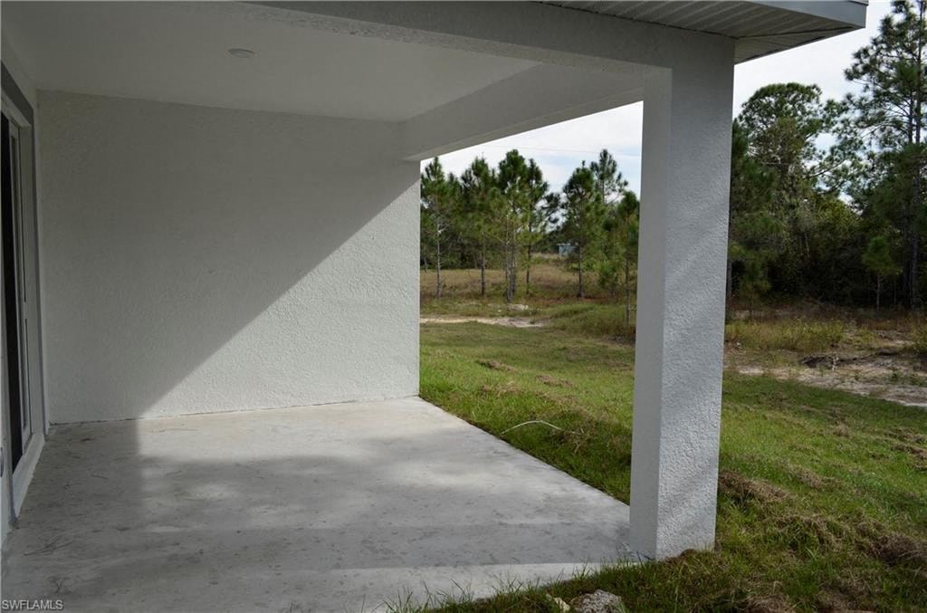 a covered porch with grass and trees in the background