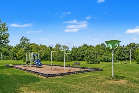 A playground with a slide, swings, and a bench is surrounded by trees.