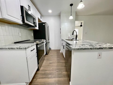 an empty kitchen with marble counter tops and white cabinets