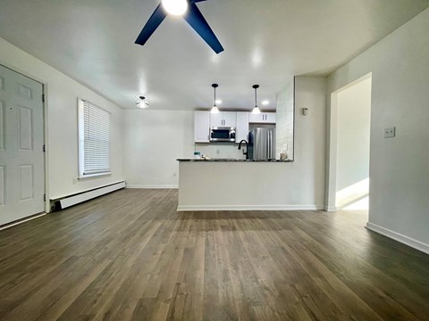 an empty living room with a kitchen in the background and a ceiling fan