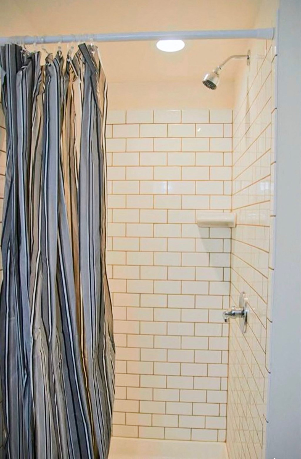 a white tiled shower with a striped shower curtain