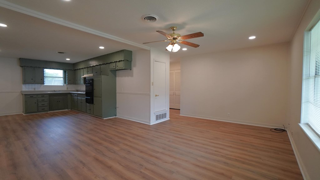 an empty living room with a ceiling fan and a kitchen