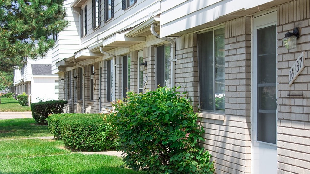 A white house with a green bush in front.