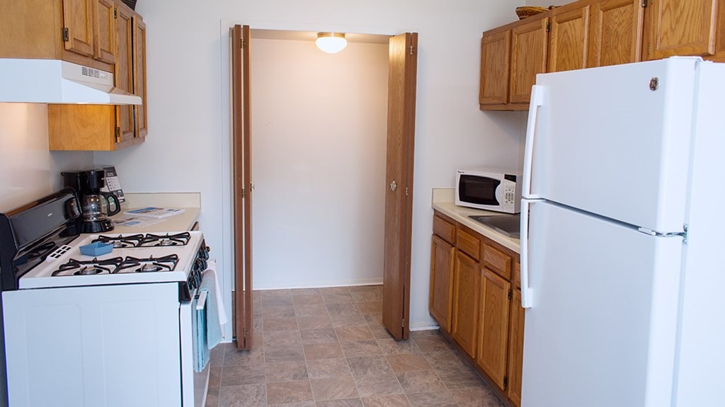 A kitchen with a white refrigerator, a white stove, and wooden cabinets.