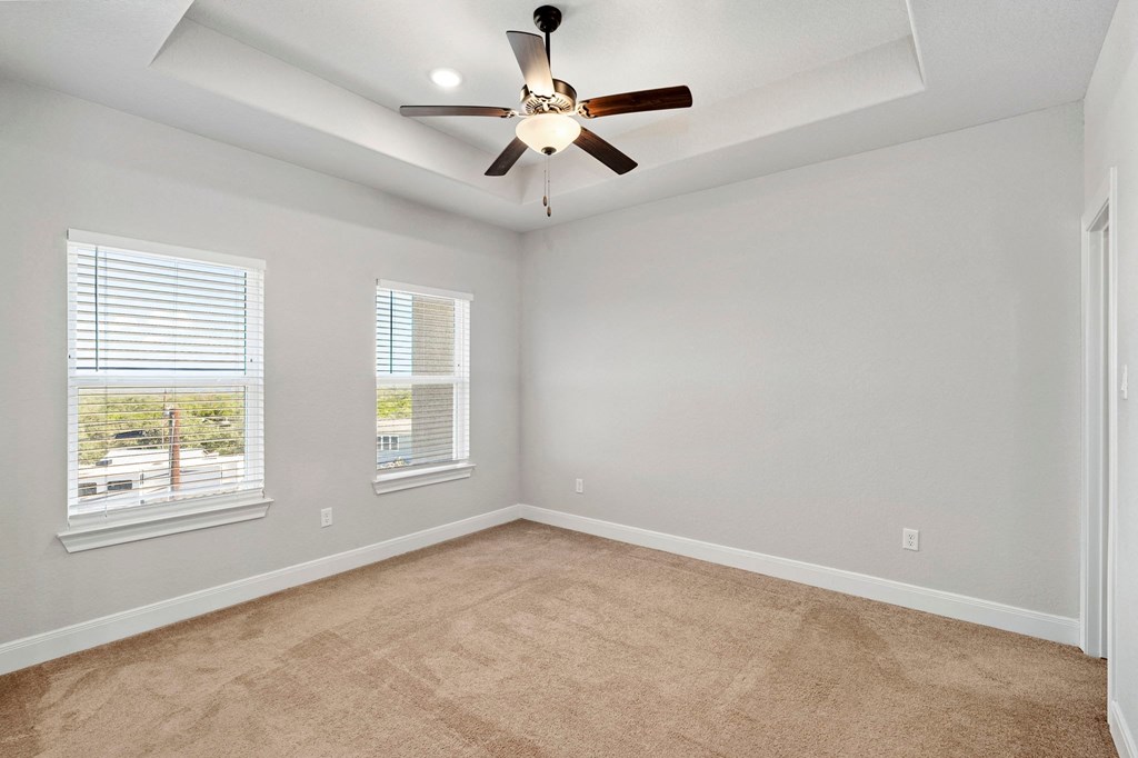 an empty living room with a ceiling fan and two windows