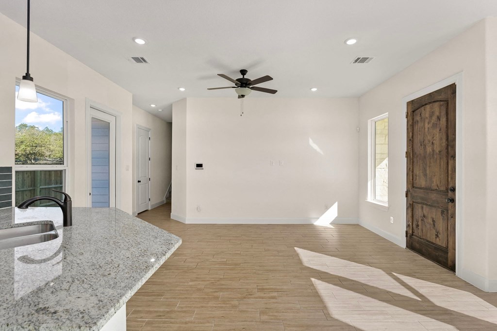 an empty living room with a kitchen and a ceiling fan
