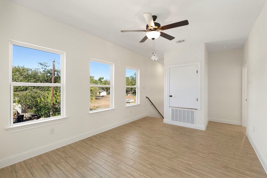 an empty living room with a ceiling fan and three windows