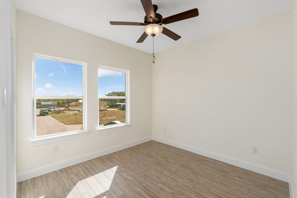 an empty living room with a ceiling fan and two windows