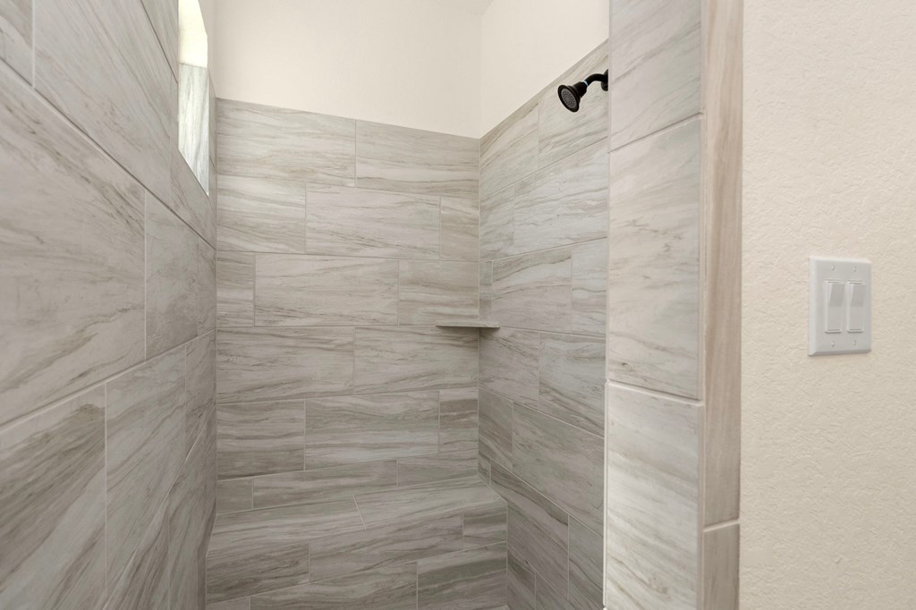 the master bathroom has a large shower with marble tiled floors and walls