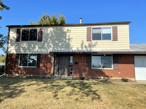 A house with a beige siding and a brick base with a white door and windows.