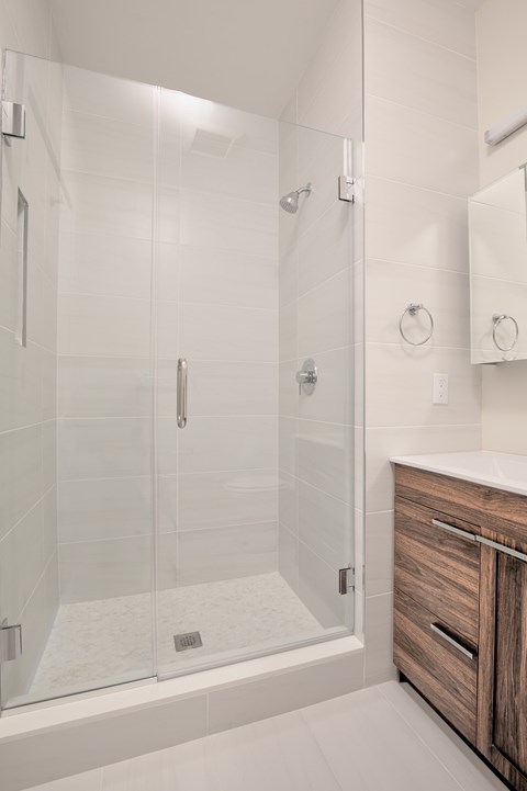 A modern bathroom with a walk-in shower and a wooden cabinet.
