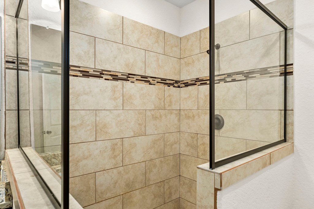 the master bathroom has a large tiled shower with a glass door