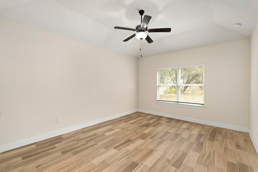 the spacious living room with hardwood flooring and a ceiling fan